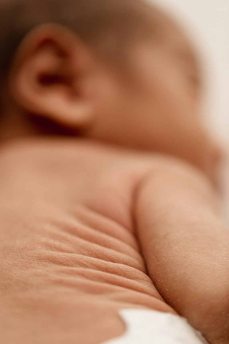 Newborn Photographer, a baby lays on chest exposing all the little rolls in his back