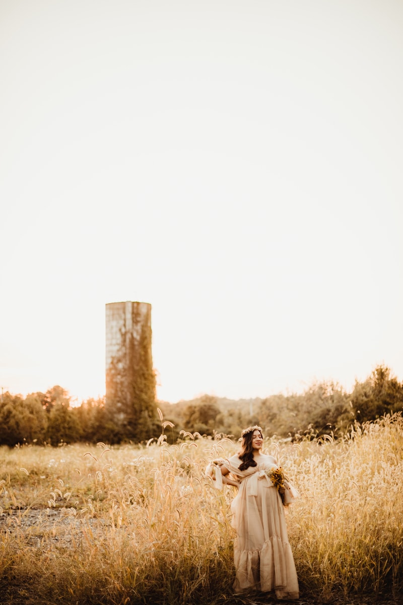 Fine Art Maternity Photographer, a young mother-to-be holds a bouquet in a field of tall grass