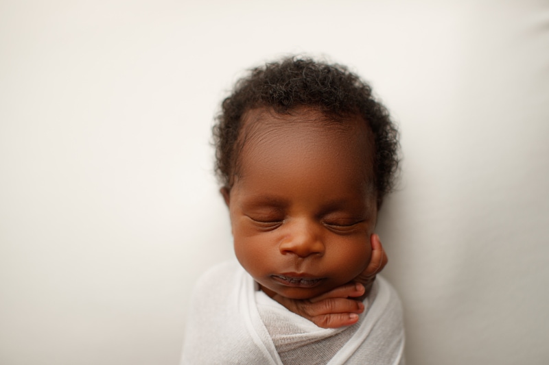 Newborn Photographer, a little baby sleeps wrapped in a blanket with full head of hair