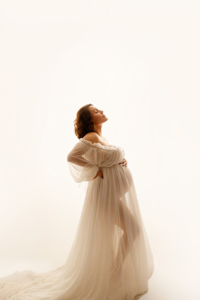 Fine Art Maternity Photographer, an expectant mother wears a tulle dress and places her hand on belly