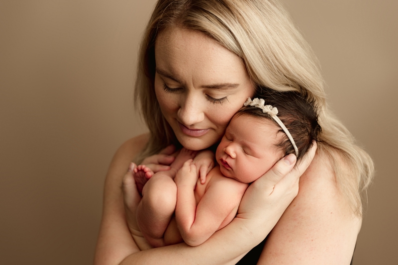 Newborn Photographer, a mother brings her baby girl close her face tenderly as she holds her