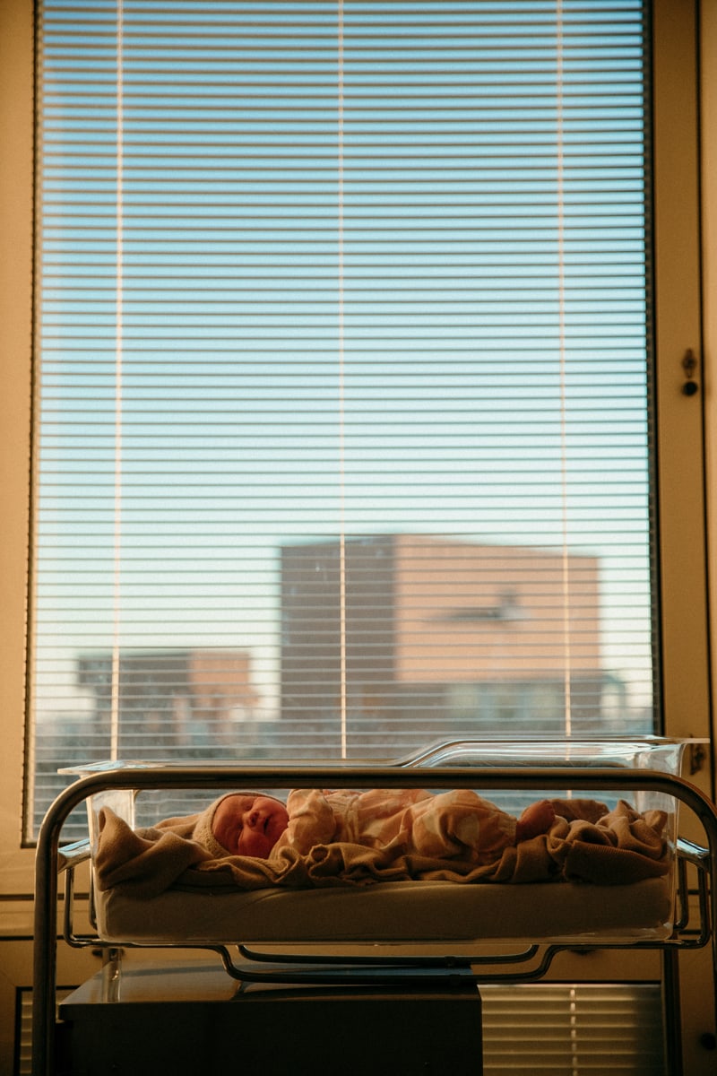 Birth Photographer, a baby lays sleeping before a window and cityscape