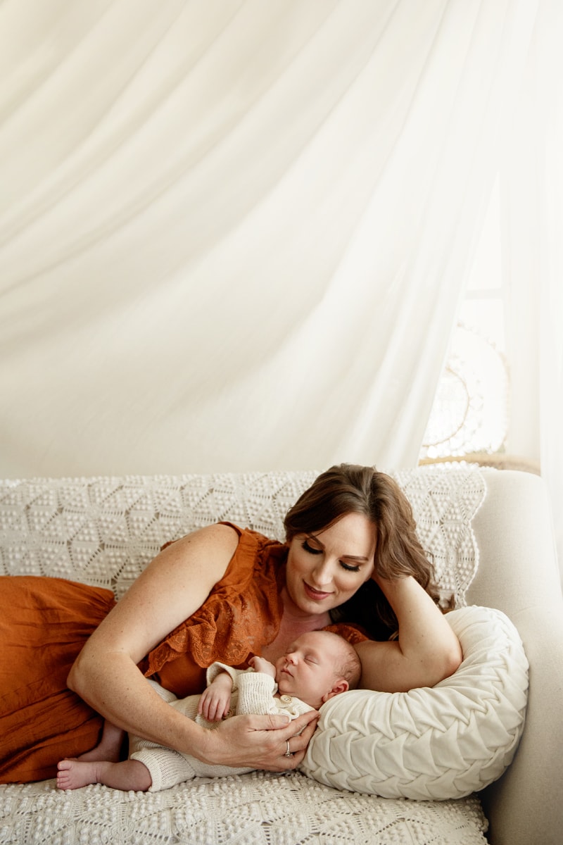 Lifestyle Photographer, mom lays on the couch holding her baby who sleeps comfortably