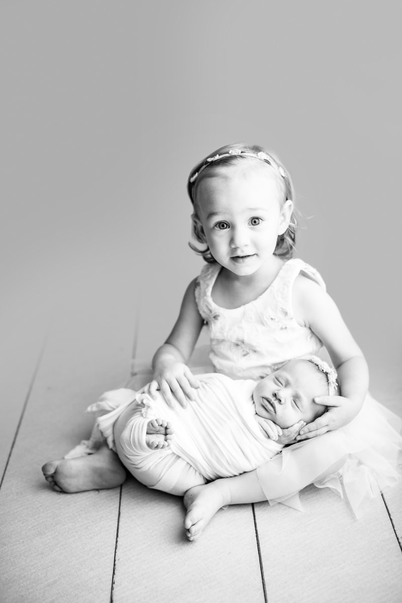 Newborn Photographer, older sister is gentle as she holds her younger sister