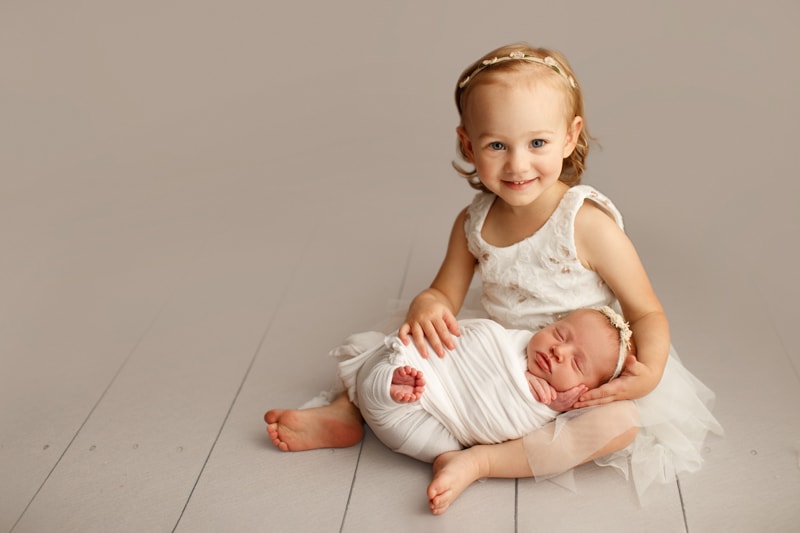 Newborn Photographer, a baby girl lays cozy on her older sister's lap, older sister is happy and smiles