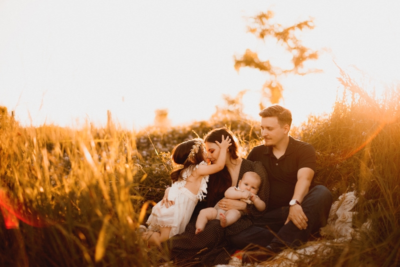 Family Photographer, a mom and dad sit with their kids, dad holds baby, mom and older sister snuggle