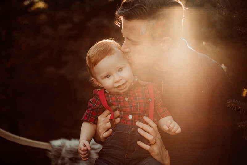 Family Photographer, a dad kisses his smiling baby boy in his arms at golden hour