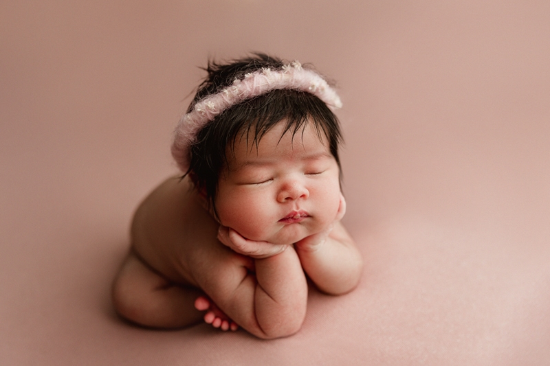 Newborn Photographer, a baby girl is propped up on her little hands, she wears a little headband around her head of hair