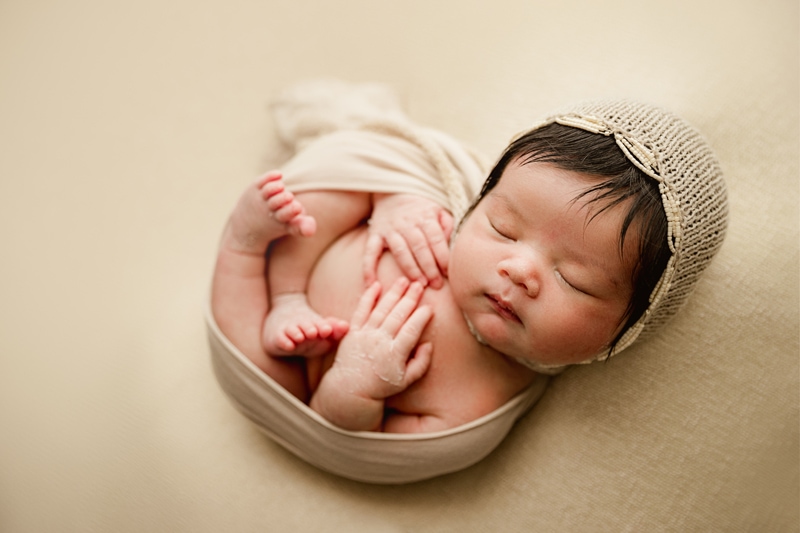 Newborn Photographer, a little baby is bundled into a ball, knit cap keeps her head warm