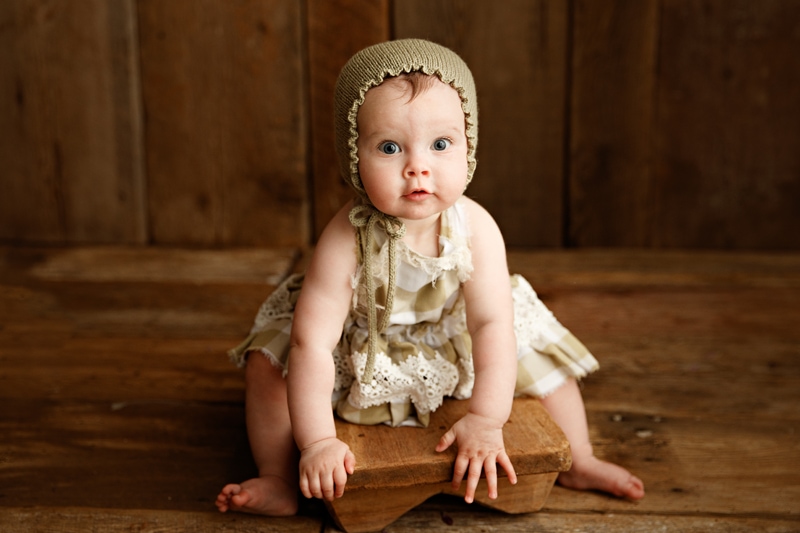 Baby Photographer, a little girl with a knit cap and dress perches on a wooden step stool
