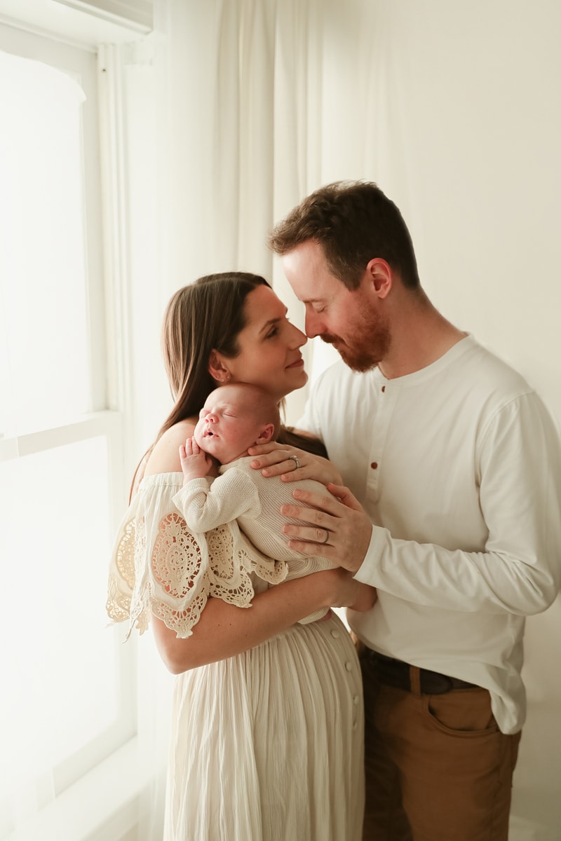 Lifestyle Photographer, mom and dad draw close nose to nose s mom holds baby