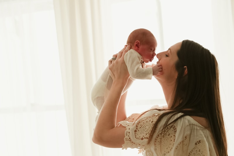Lifestyle Photographer, a mother holds her newborn baby her face tenderly