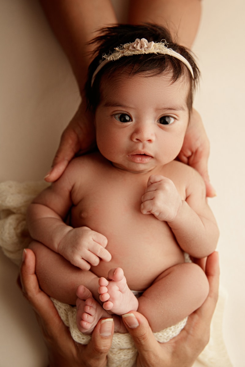 Newborn Photographer, mom and dad's hands both hold their newborn baby girl, she is wide-eyed and alert