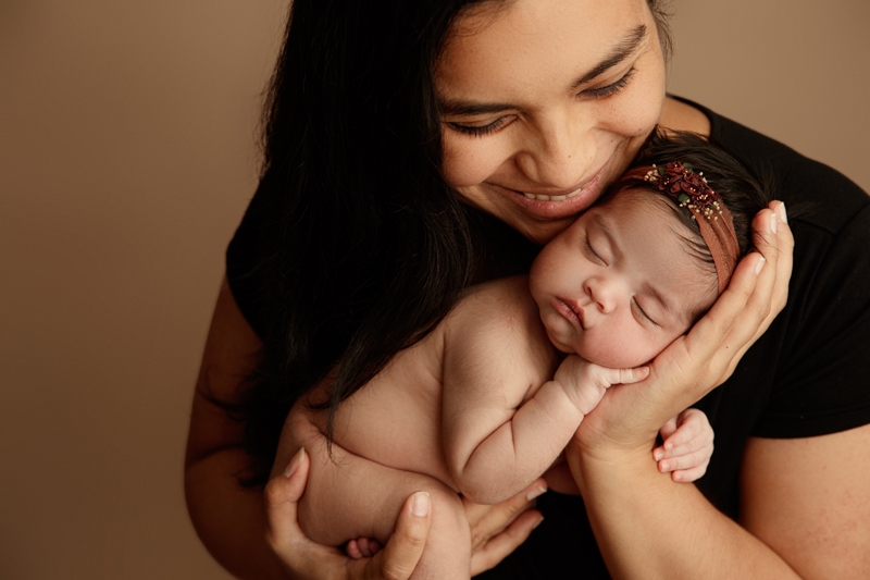 Newborn Photographer, a young mother smiles and holds her baby closer to her chest and face