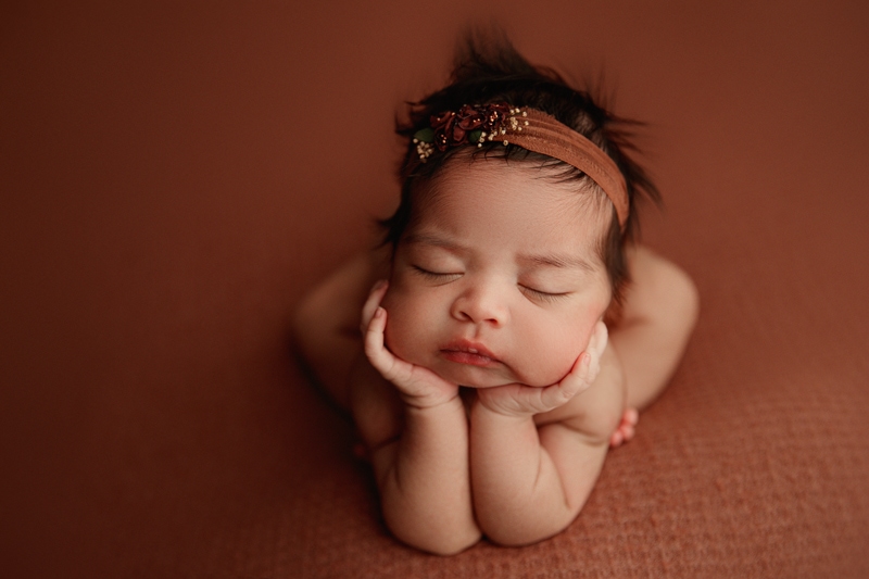 Newborn Photographer, a baby girl wears a decorative headband while napping on a blanket