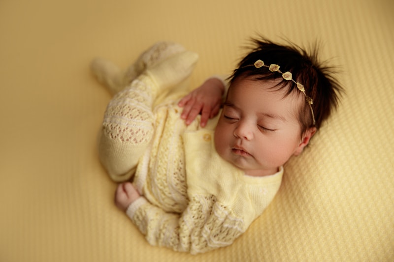 Newborn Photographer, a baby naps on a knit blanket, with a head band on her full head of hair