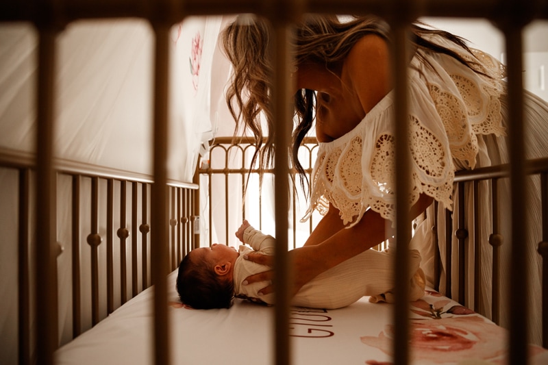 Lifestyle Photographer, Mom lays baby down in the crib to sleep