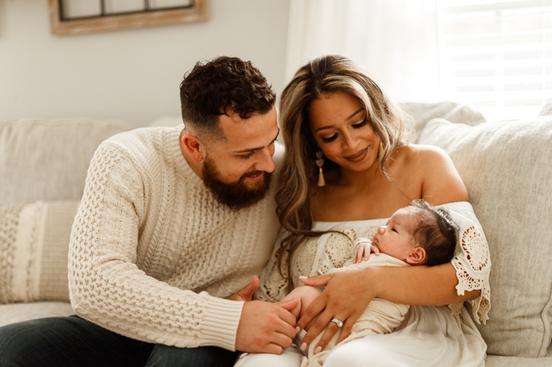 Lifestyle Photographer, mom holds baby as dad huddles in admiring her