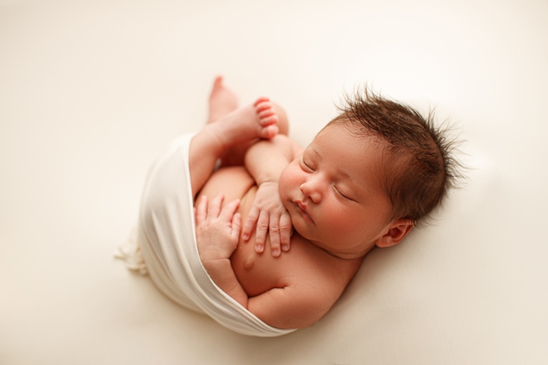 Newborn Photographer, a little baby is sleeping, hands on chest, and legs near chest also