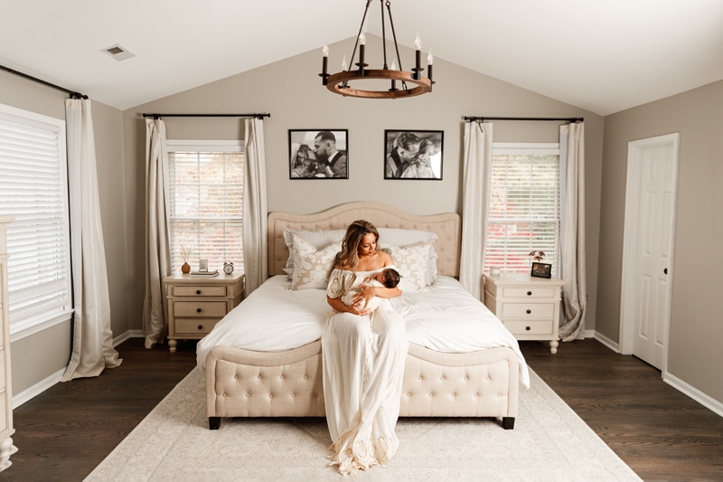 Lifestyle Photographer, Mom holds baby in her arms as she sits on her bed