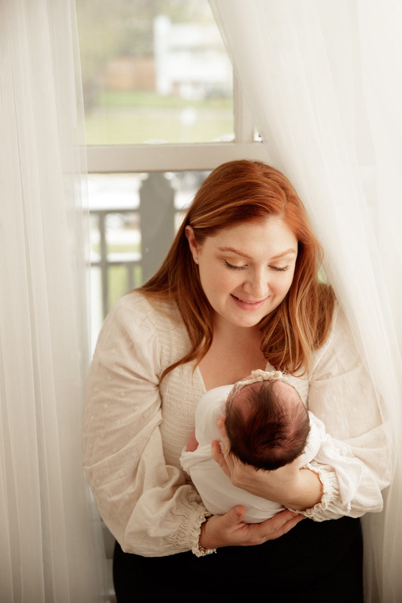 Lifestyle Photographer, mom holds her baby as she sits in the window sill