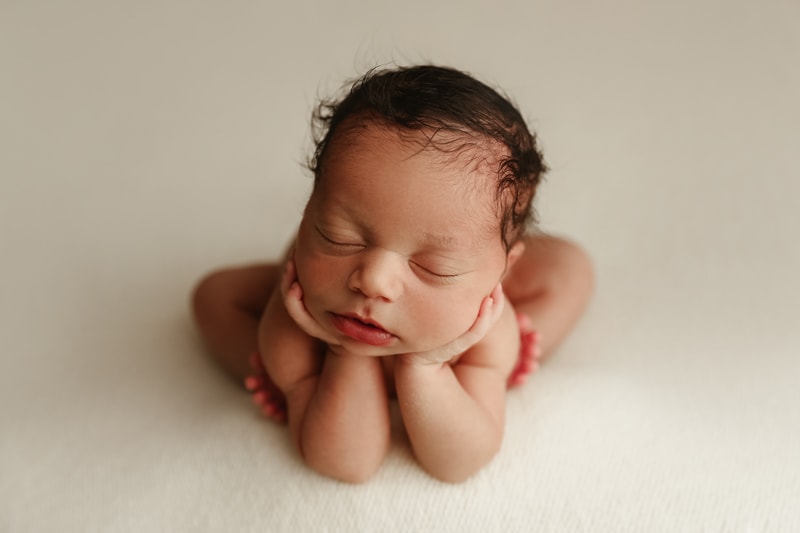 Newborn Photographer, a little baby sits propped up, his arms underneath his chin