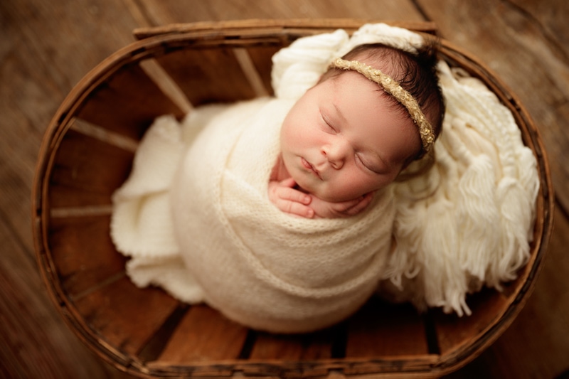 Newborn Photographer, a baby girl is swaddled in a blanket and asleep in a basket