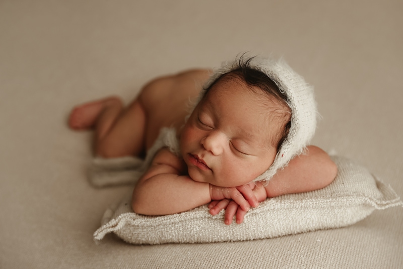 Newborn Photographer, a little baby lays sleeping with hands propped under head, a pillow beneath her