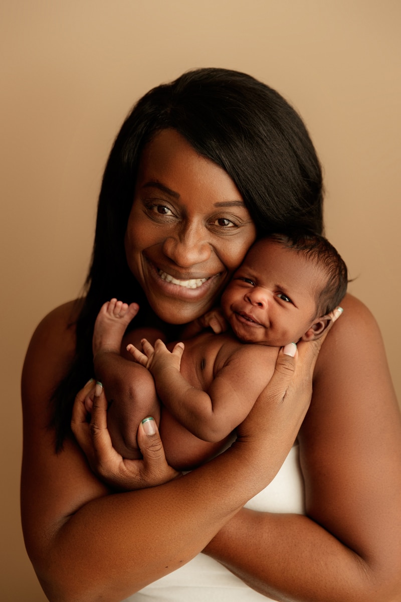 Newborn Photographer, a mother has a big smile as she presents her baby, she snuggles him close to her chest