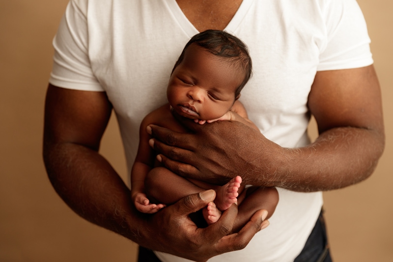 Newborn Photographer, dad holds his newborn baby close to chest while baby sleeps