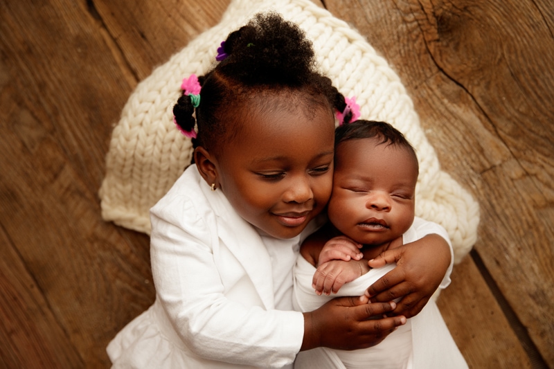 Newborn Photographer, older sister smiles as she snuggles with her new baby sibling
