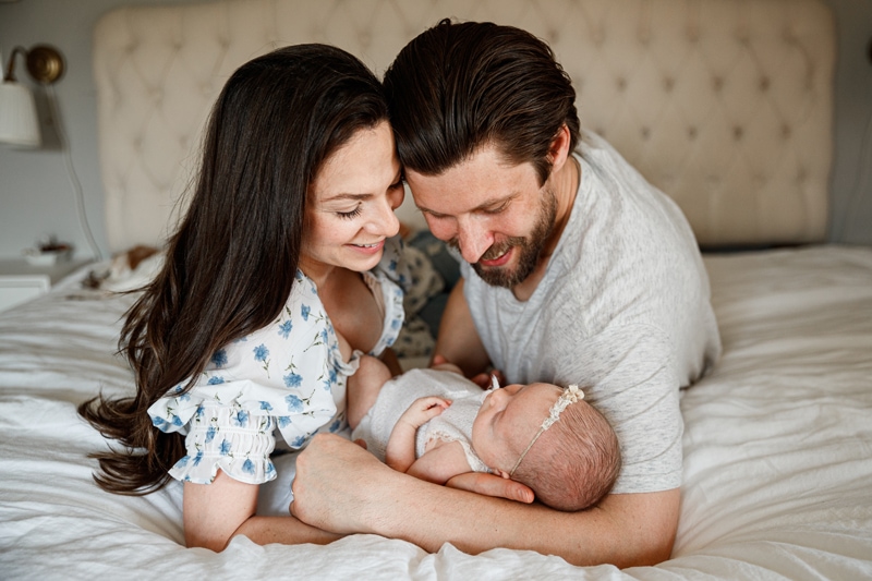 Lifestyle Photographer, mom and dad lay on the bed holding baby and admire their baby girl