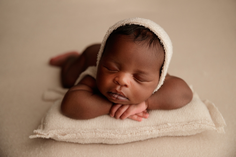 Newborn Photographer, a baby lays asleep on belly with arms propping up head, baby is on a knit cushion
