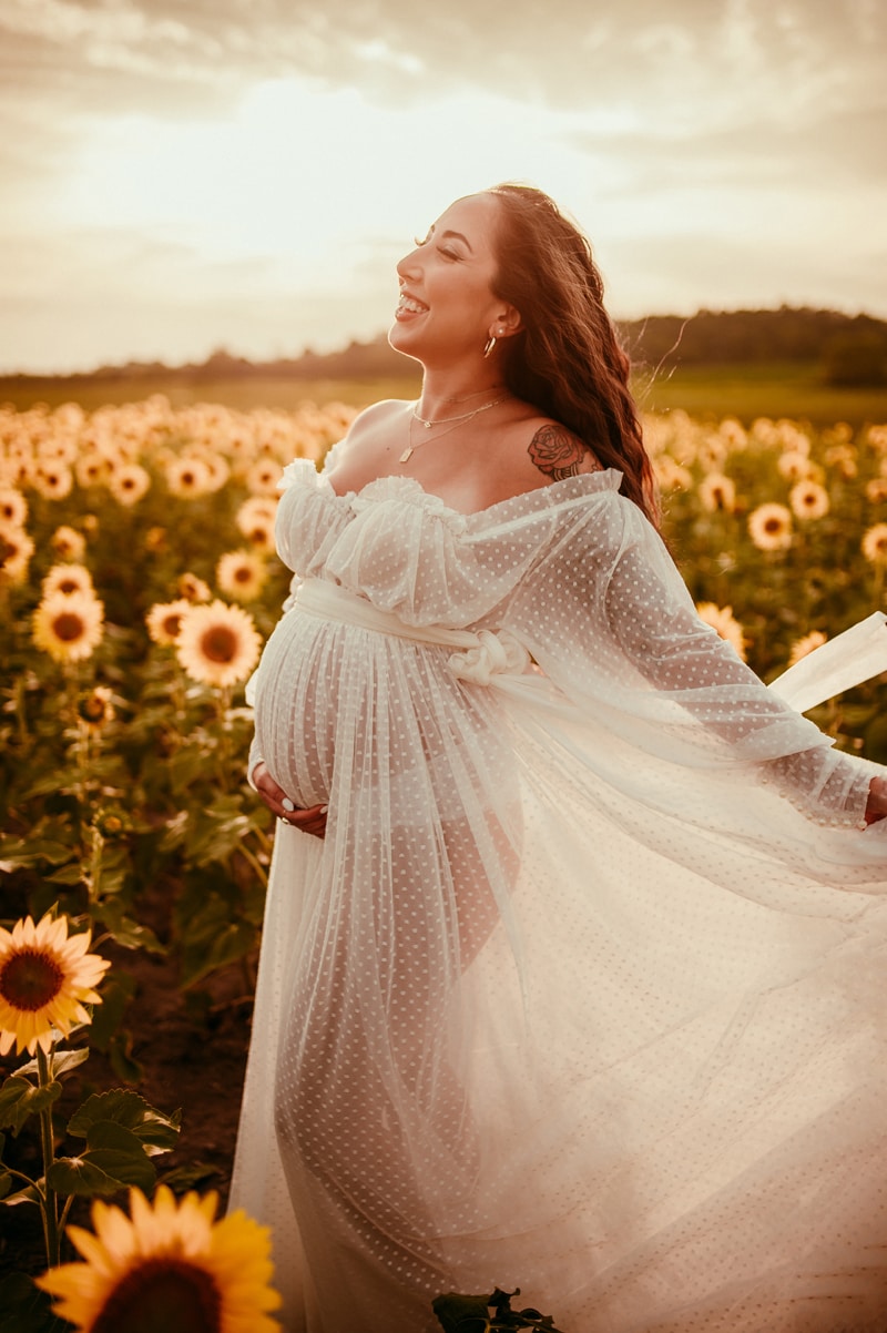 Fine Art Maternity Photographer, an expectant mother wears a tulle dress and walks through a field of sunflowers