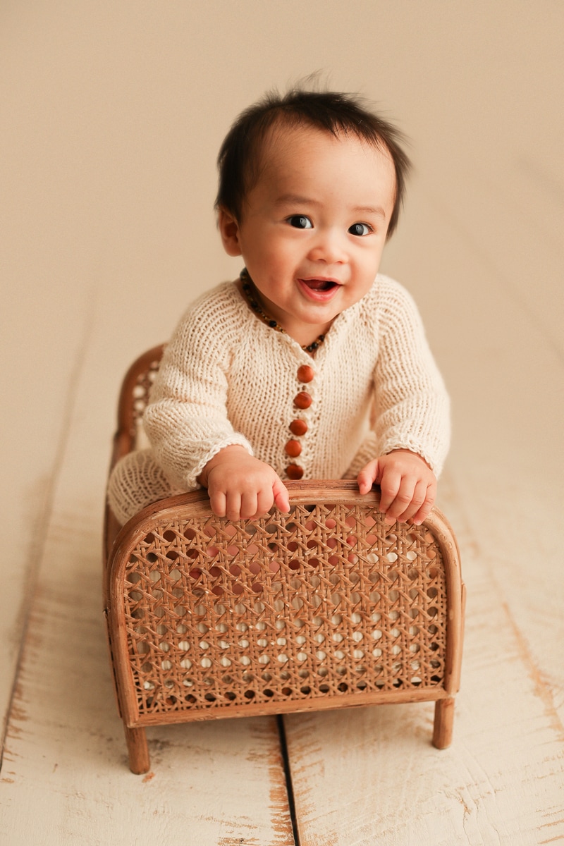 Baby Photographer, a little boy leans up a small wicker crib