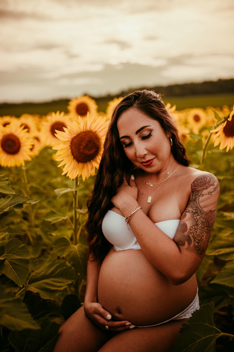 Fine Art Maternity Photographer, a mother exposes her belly, she is in her underwear and sits in a field of flowers