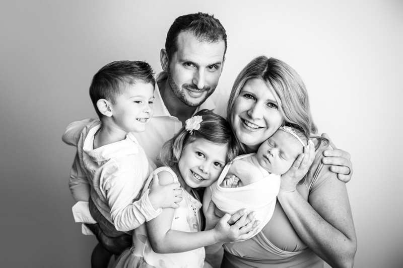 Newborn Photographer, a family celebrates their new baby sister, mom , dad, older brother and older sister all smile