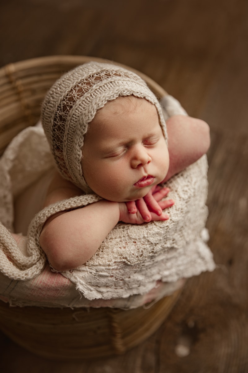 Newborn Photographer, baby wears a knit cap and sleeps perched on the edge of a basket