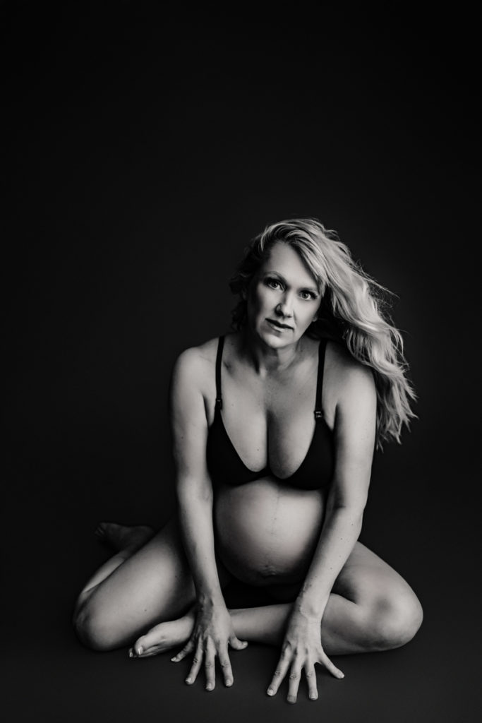 Fine Art Maternity Photographer, a mother in a swimsuit sits perched on the floor, her baby bump exposed