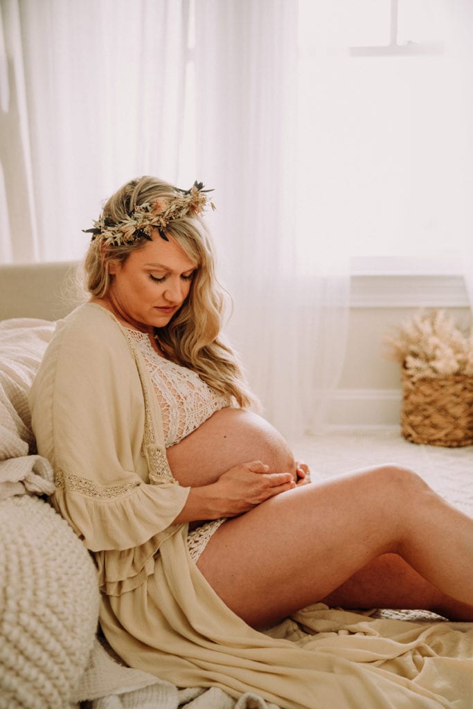 Fine Art Maternity Photographer, a mother wears a dress open to expose her pregnant belly, she reclines in her living room