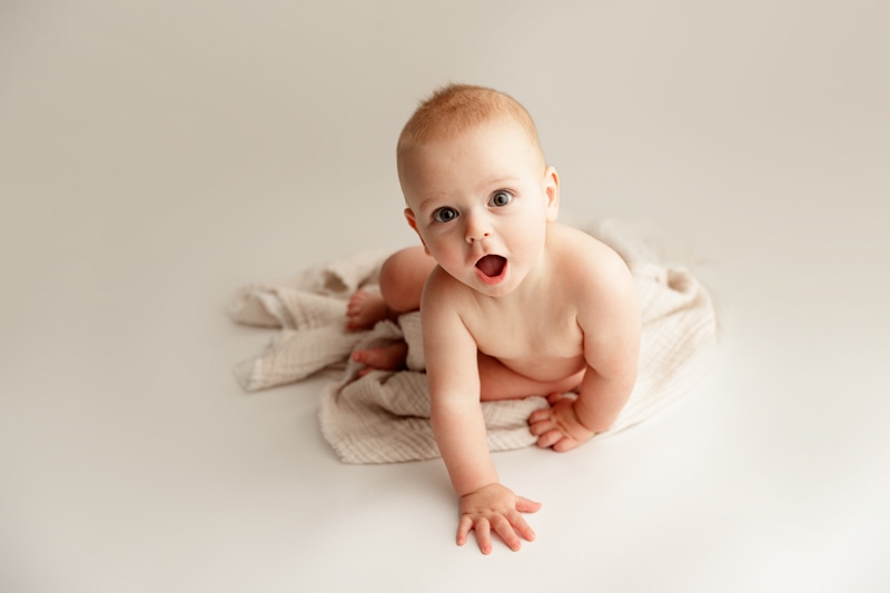 Baby Photographer, a baby boy sits on blanket and begins to crawl