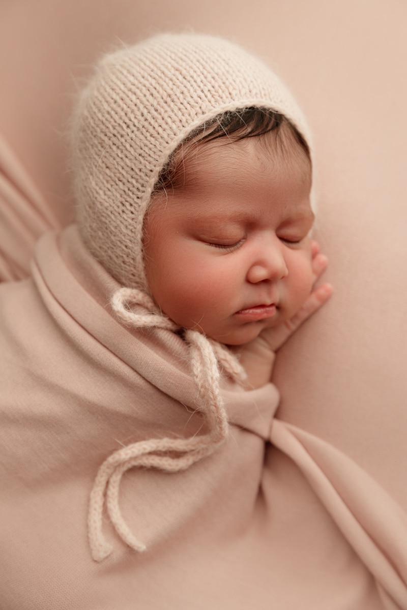 Newborn Photographer, baby girl lays on her hands asleep wrapped in linens