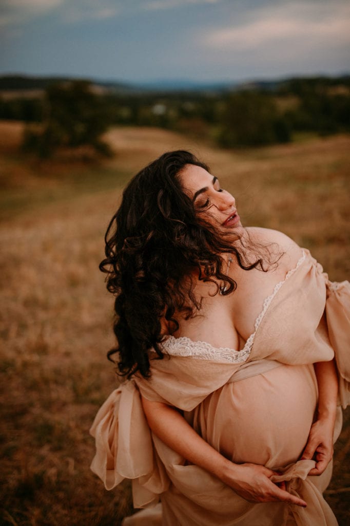Maternity Photographer, a pregnant woman stands in a field at sunset