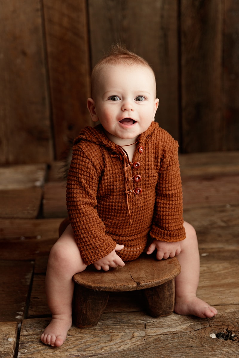 Baby Photographer, a baby boy sits on a wooden stool in a rustic cabin