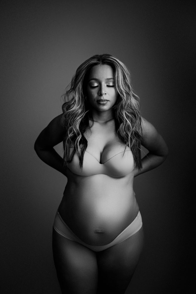 Fine Art Maternity Photographer, an expectant mother holds her hands on her back in her underwear