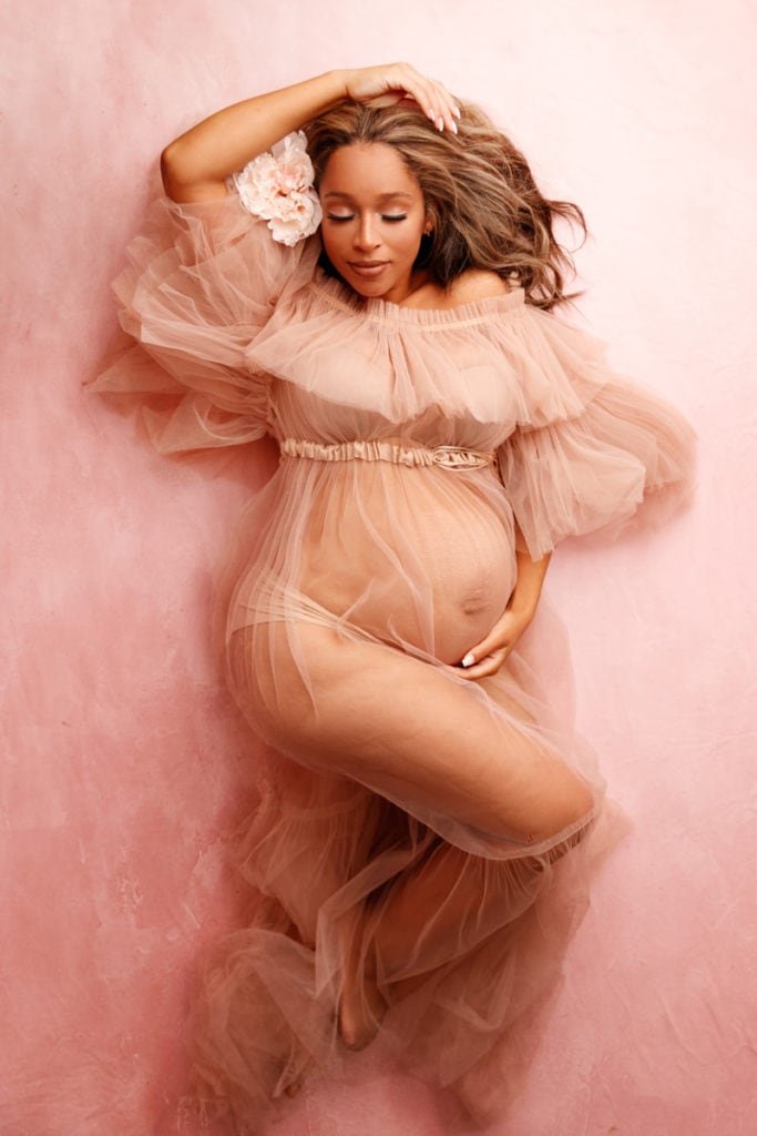 Fine Art Maternity Photographer, an expecting mother wears a tulle dress and lays down with confidence, flowers in her hair