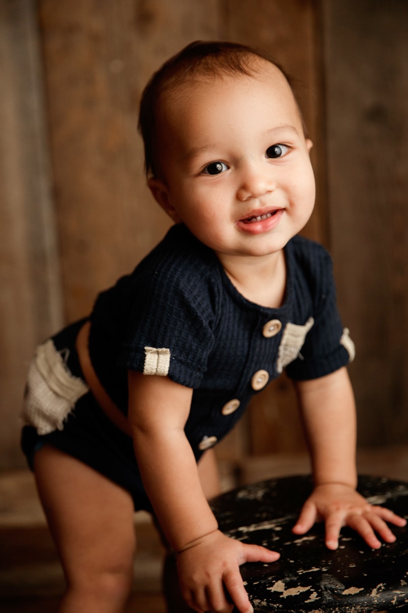 Baby Photographer, baby boy smiles as he leans on stool as he stands up