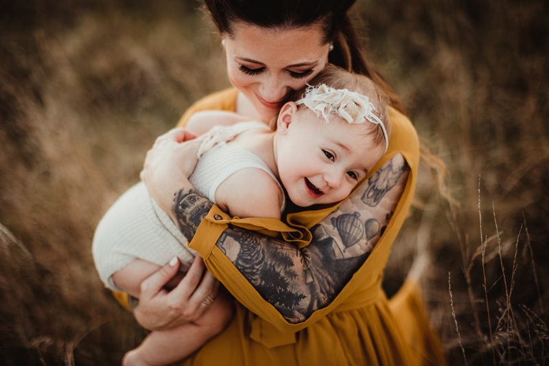 Family Photographer, a mother holds her baby close, both smile outside