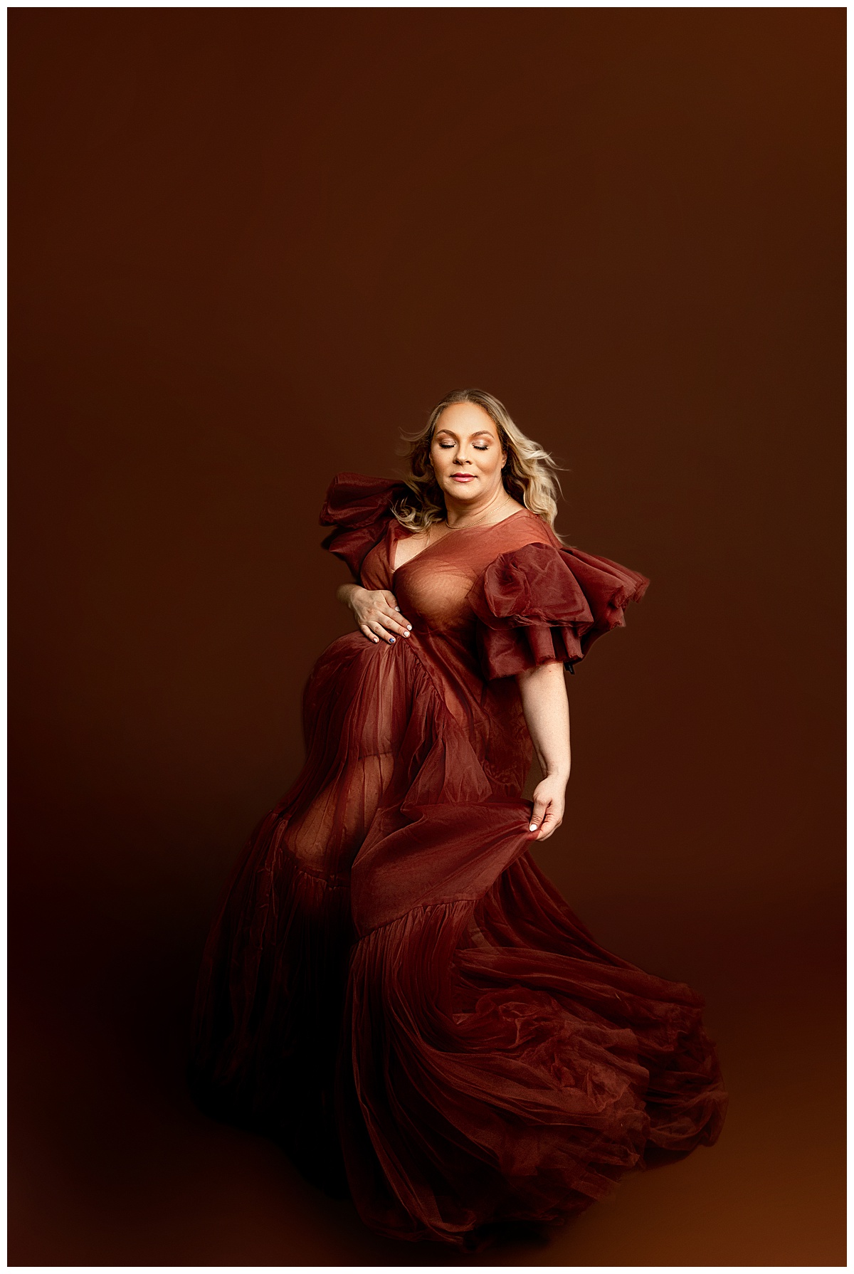 Woman dances with pregnant belly in maroon gown for Norma Fayak Photography.