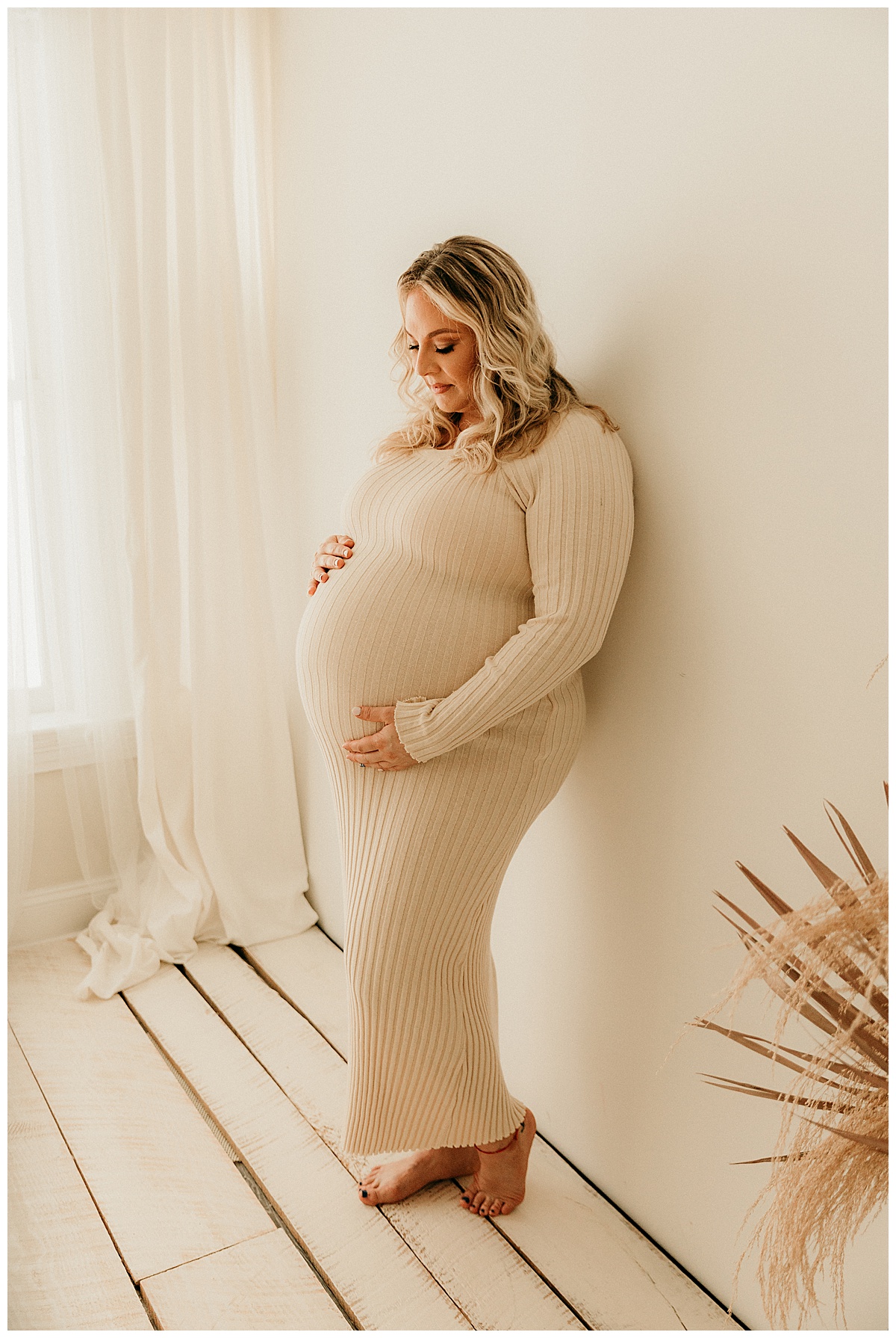 Proud mama looks down and miracle pregnant belly against wall for Norma Fayak Photography.Norma Fayak Photography.